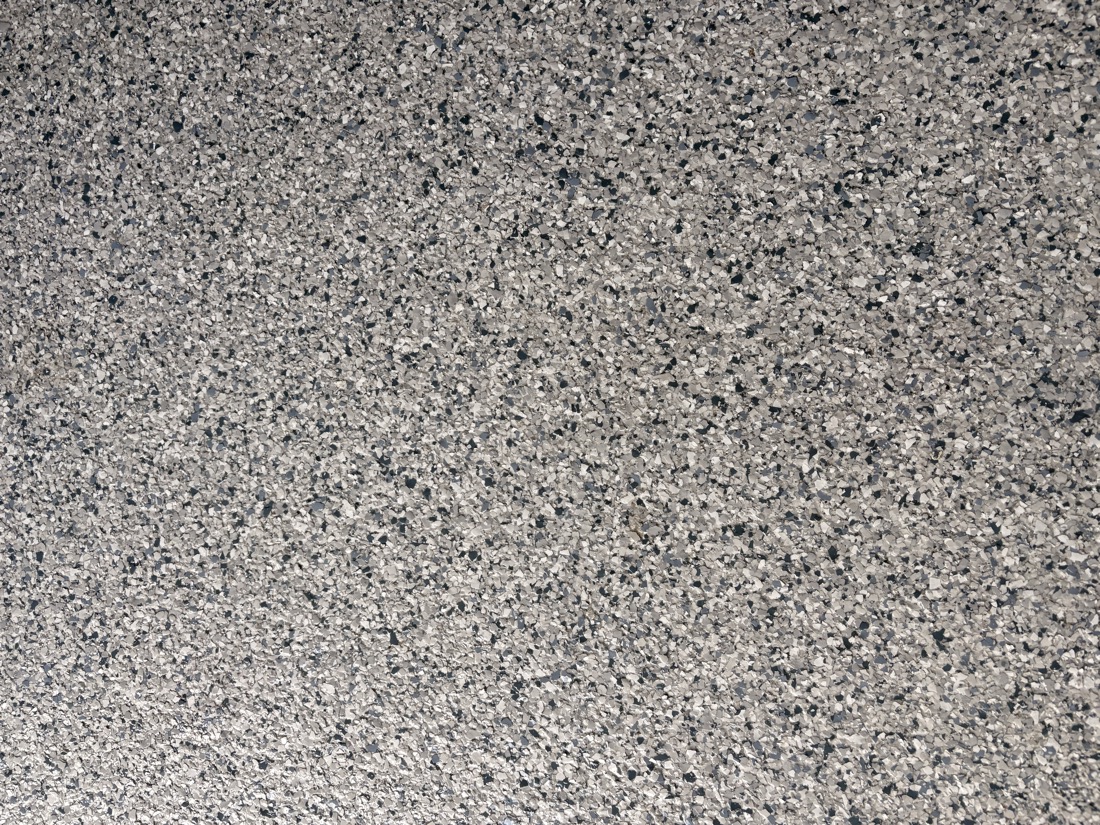 Close-up of the flake blend: white, light grey, charcoal and slate-blue vinyl chips broadcast to refusal and sealed flat.