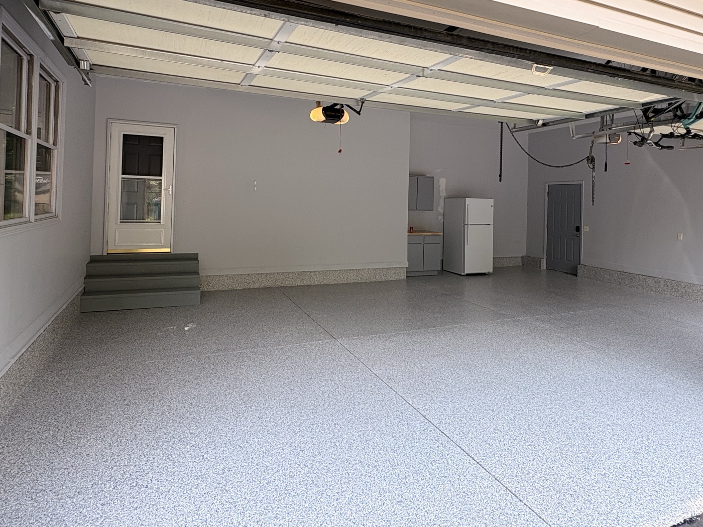 Three-car garage in Tipton, Michigan with a grey and blue flake epoxy floor, sealed and reflecting the daylight from the open door.